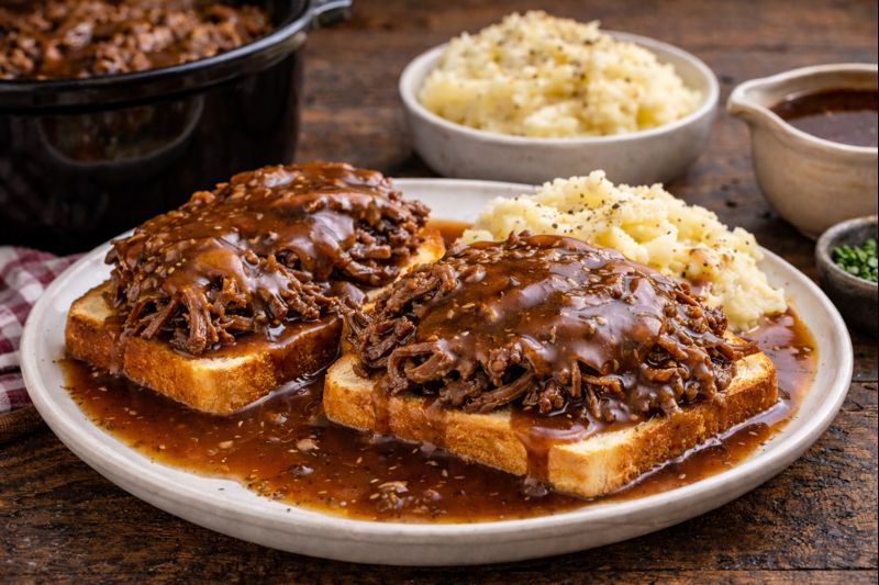 Open-faced hot beef sandwiches topped with rich gravy and served with mashed potatoes on a rustic table